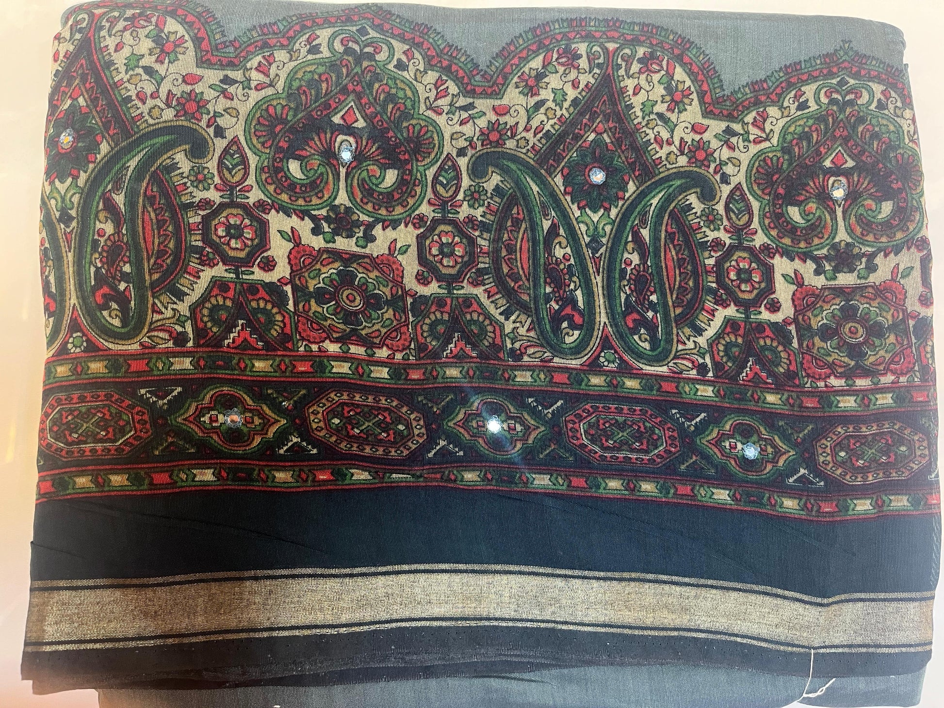 Decorative fabric with intricate paisley patterns in green, red, and black on a beige background.